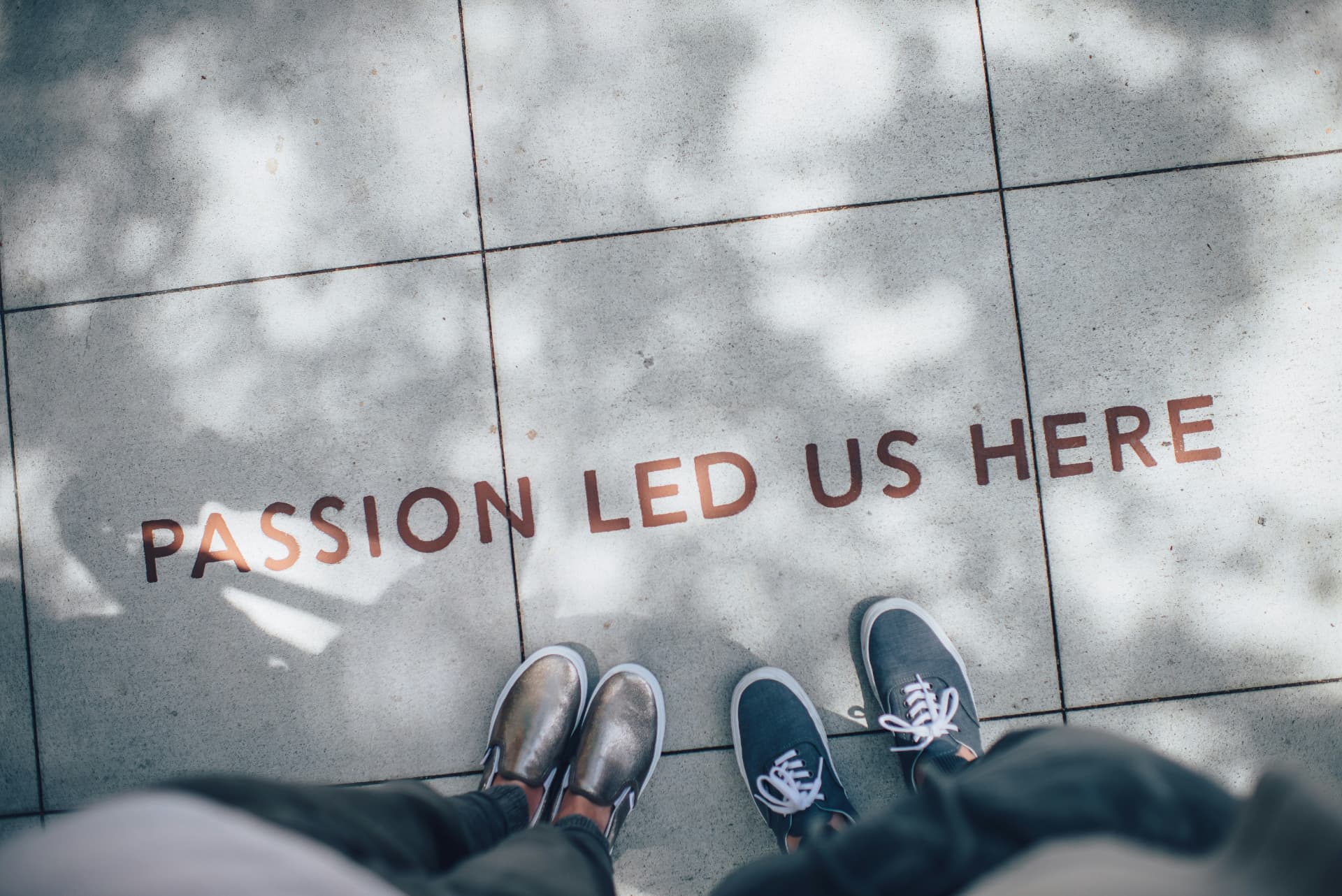 Overhead view of two people standing on pavement stencilled with the words Passion Led Us Here