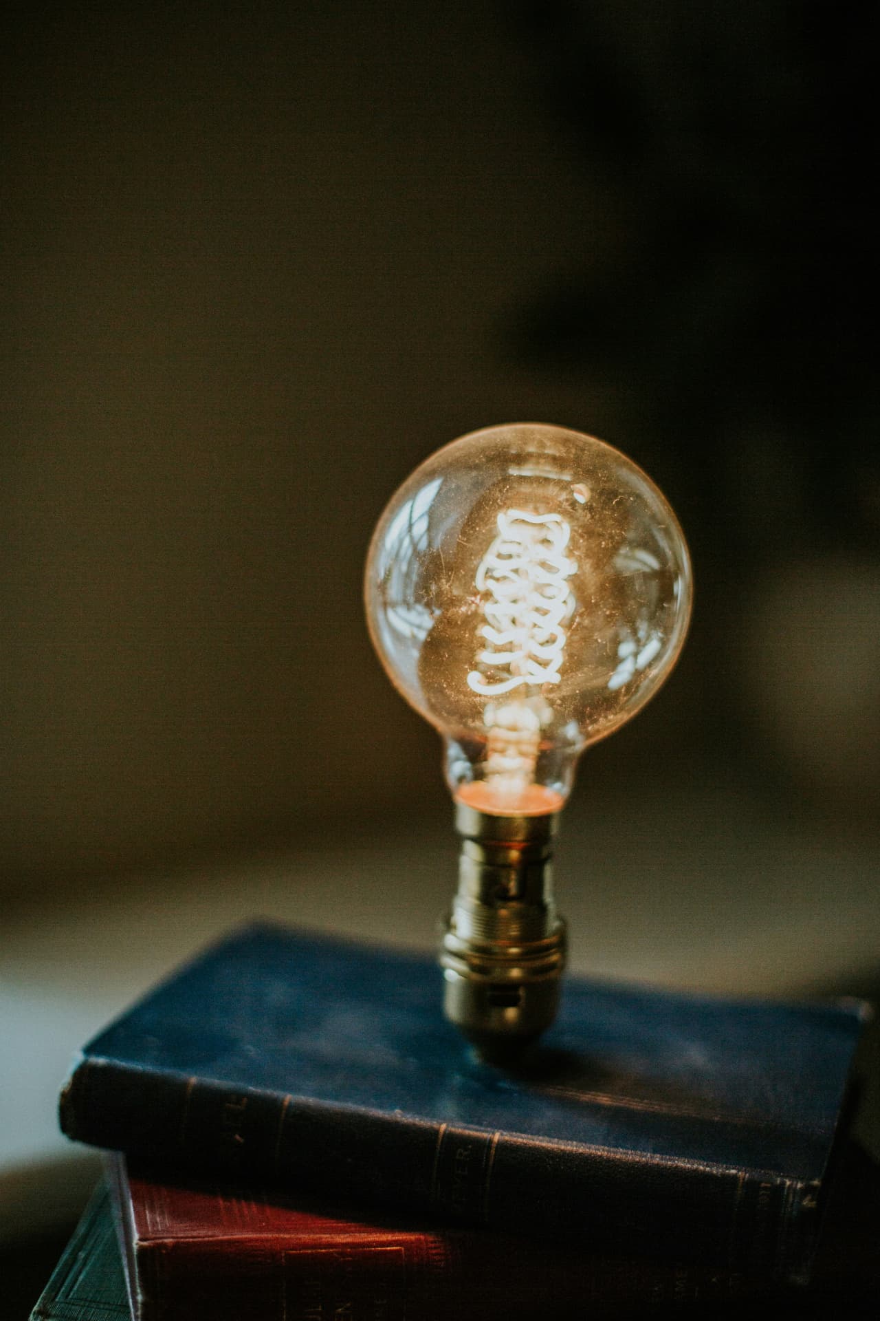 A glowing filament lightbulb resting on a stack of worn hardcover books