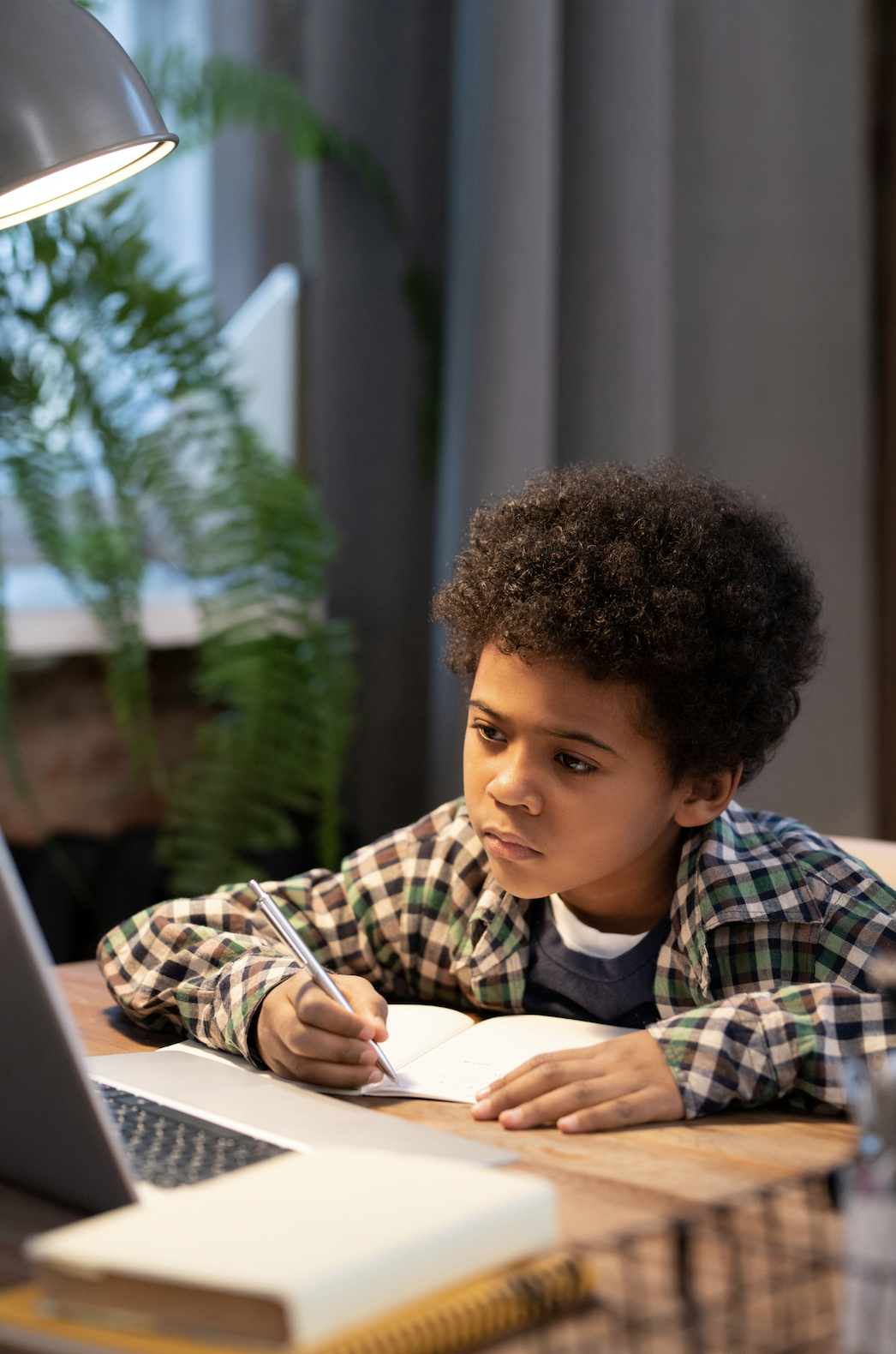 A focused young student writing in a notebook beside a laptop