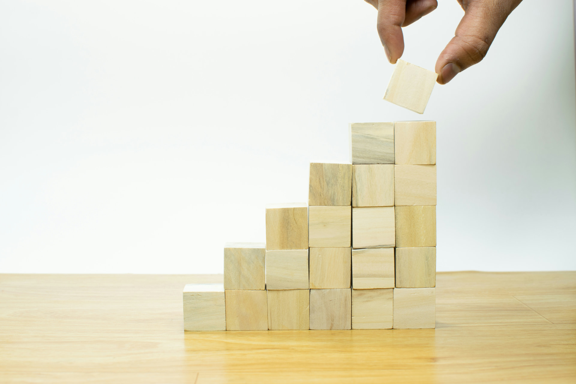 A hand placing a wooden block to build a rising staircase
